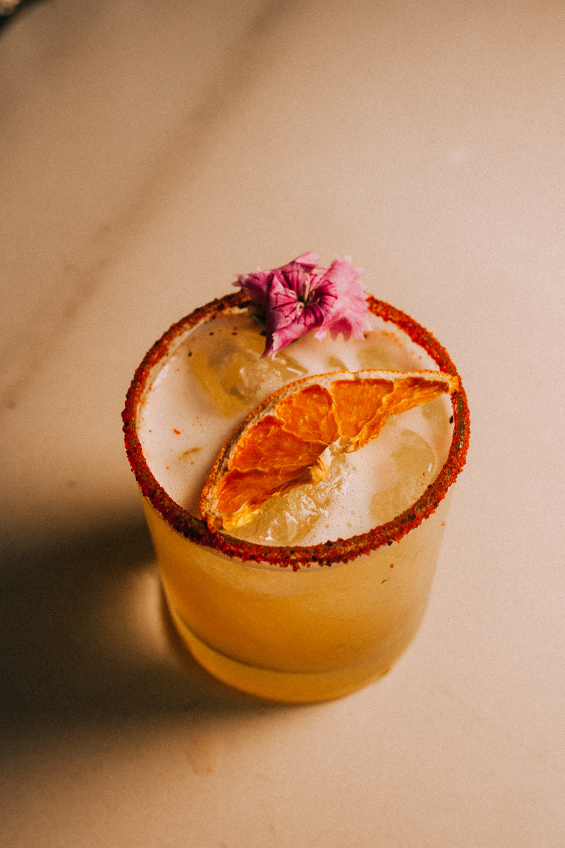 Citrus cocktail on the rocks with a chili-salt rim, dried orange and an edible flower