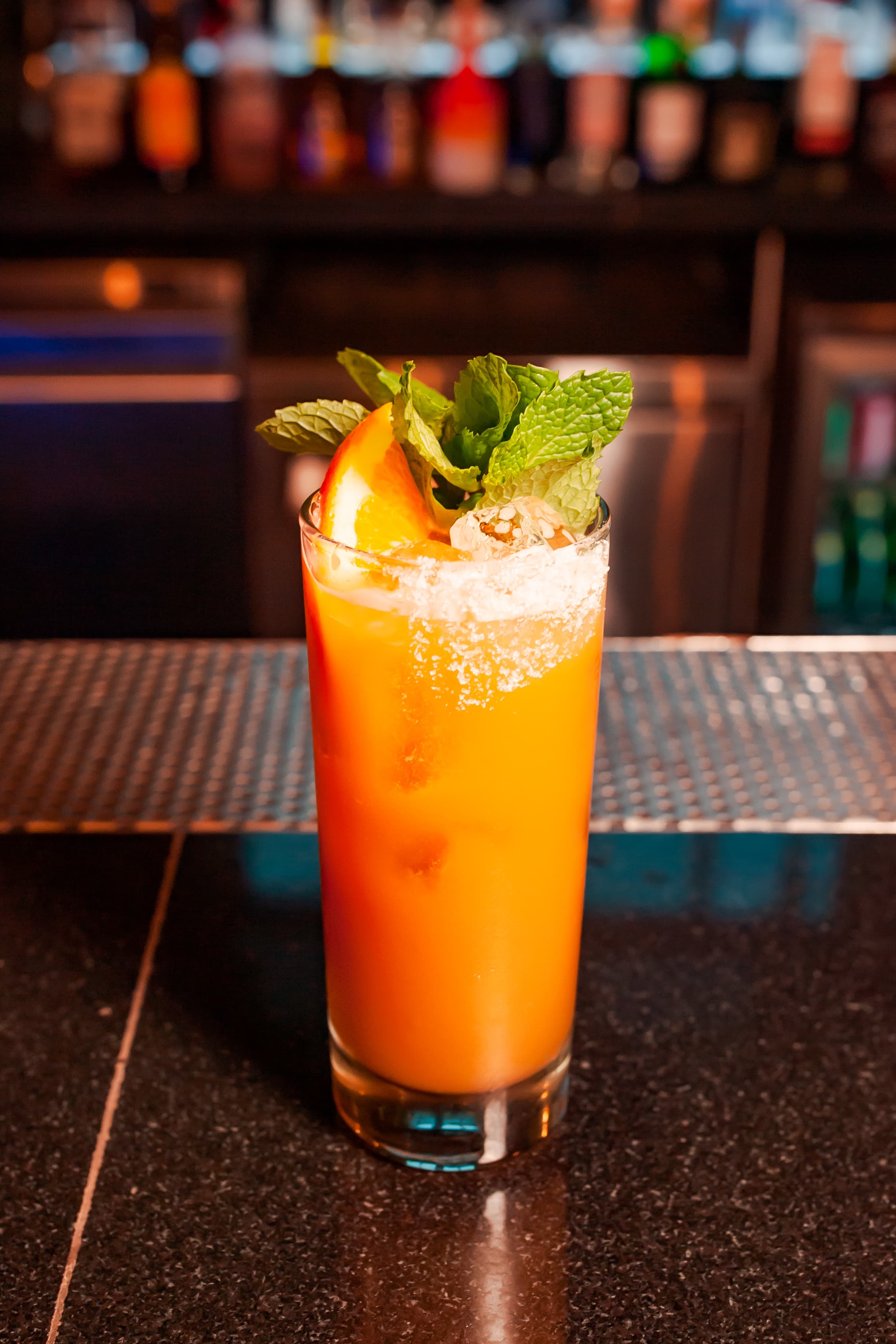 Tall orange cocktail with a sugared rim, orange wedge and fresh mint on a bar